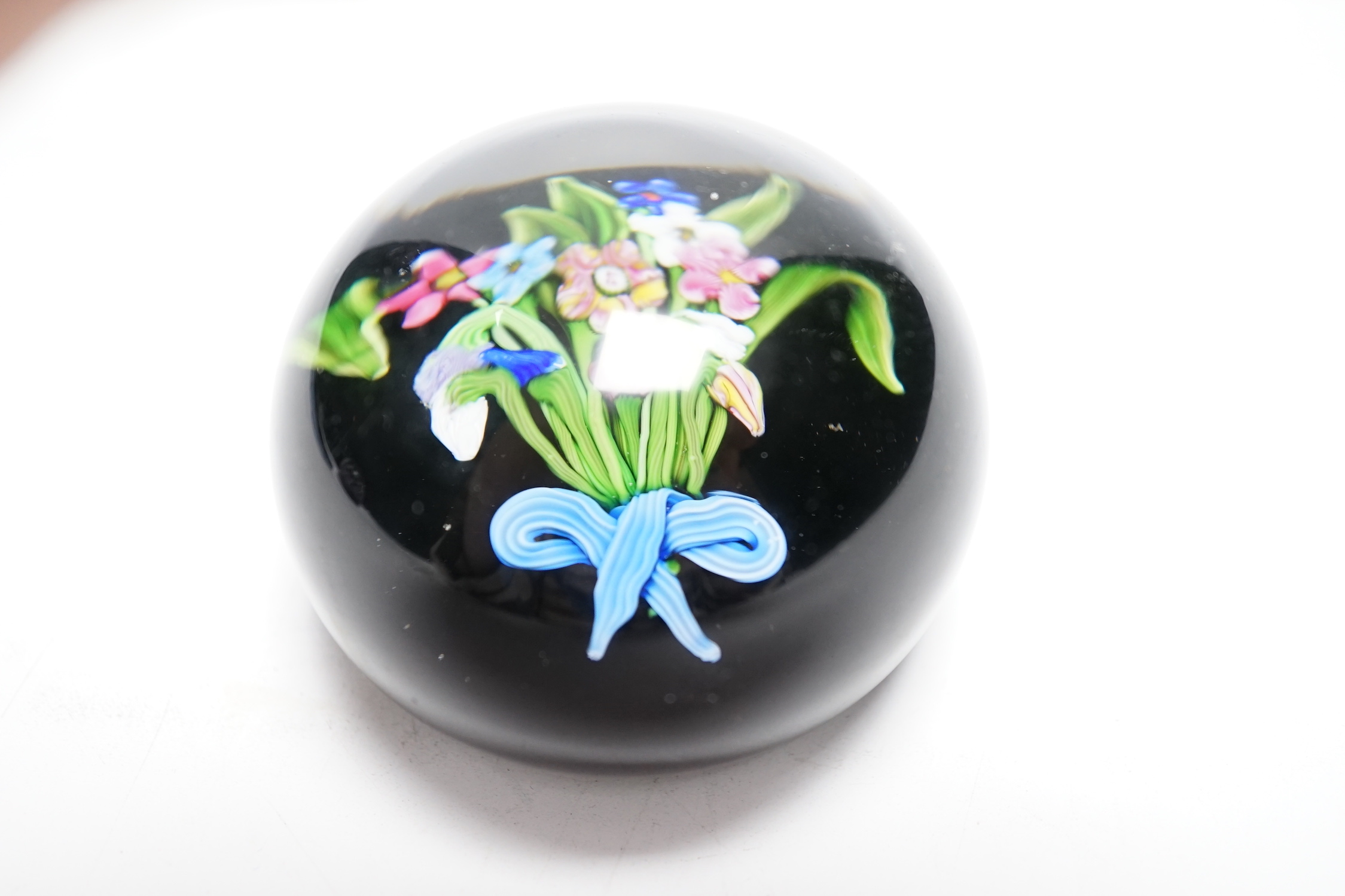 A Paul Ysart ‘small flower bouquet’ glass paperweight, pre-war Moncrieff period, ‘PY’ cane, the bouquet with a blue and white tied ribbon, black opaque ground, rough pontil, 6.5cm